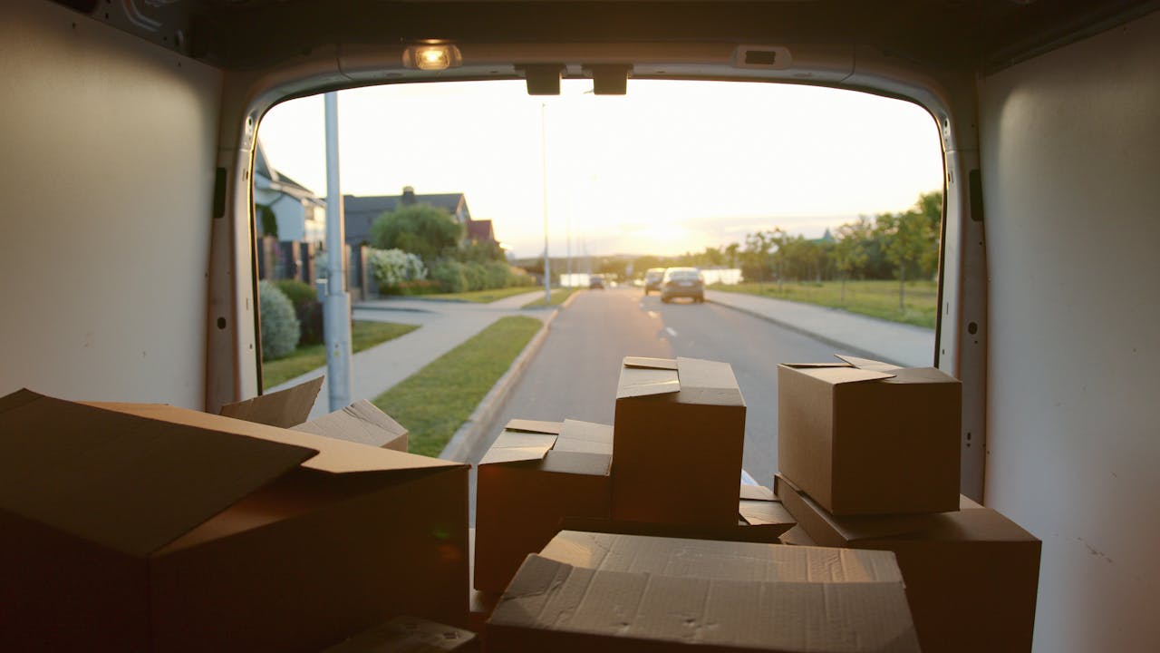 gallery-6 A scenic view from a delivery van loaded with cardboard boxes at sunset on a suburban street.
