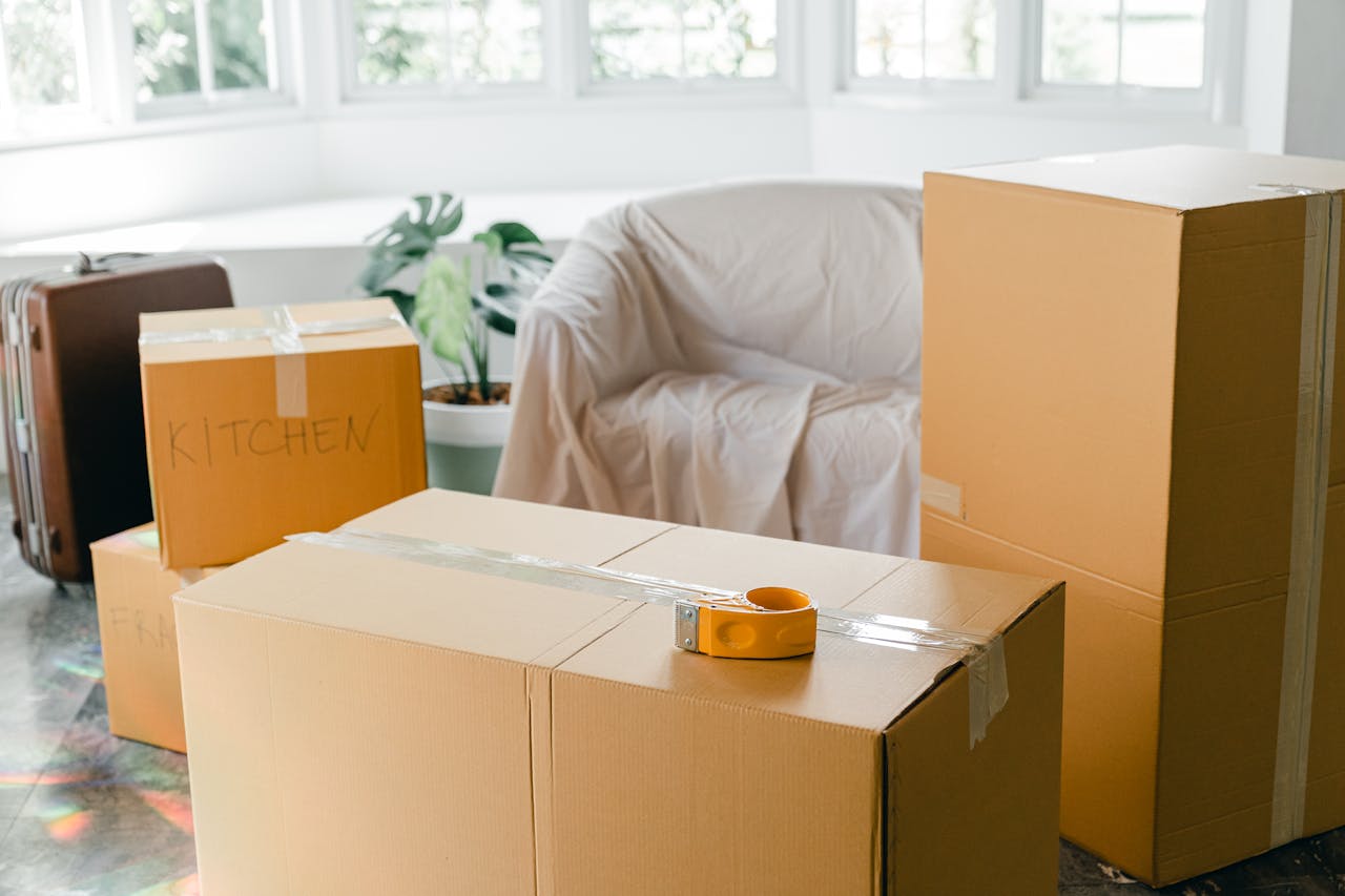 why-choose-us Cardboard boxes labeled 'Kitchen' in sunlit living room, ready for relocation.